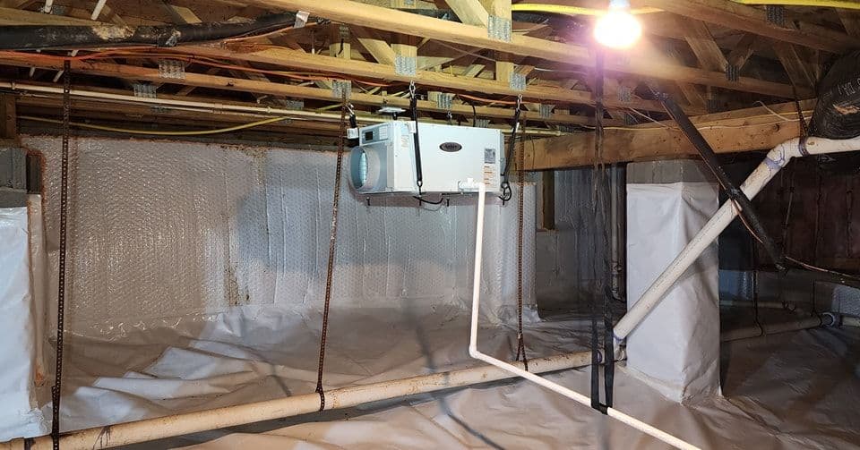 Crawl space with dehumidifier, insulated walls, and moisture barrier for home maintenance.