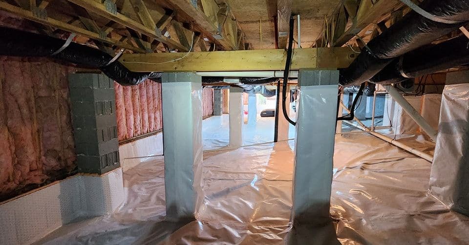 Interior of a basement with insulation, plastic sheeting, and support columns visible.
