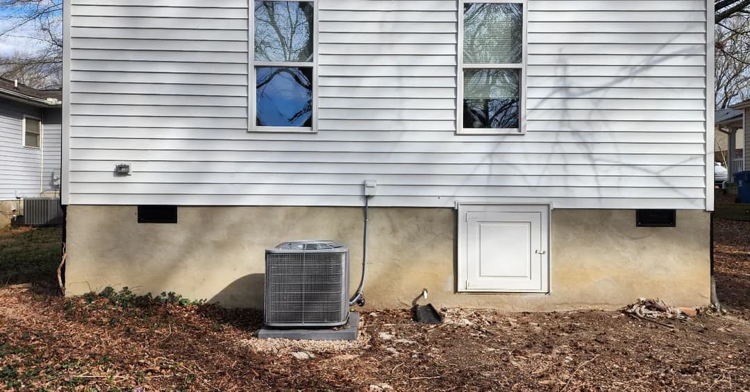 Air conditioning unit beside a house with white siding and two windows.