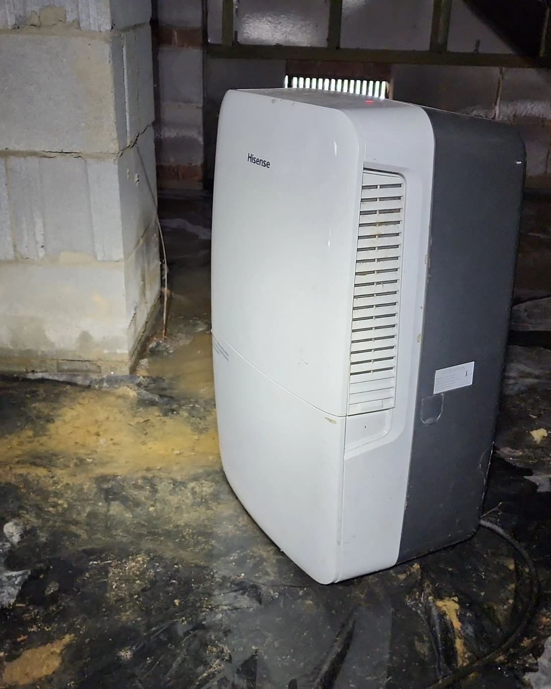 Dehumidifier in a basement with water damage and exposed concrete walls.