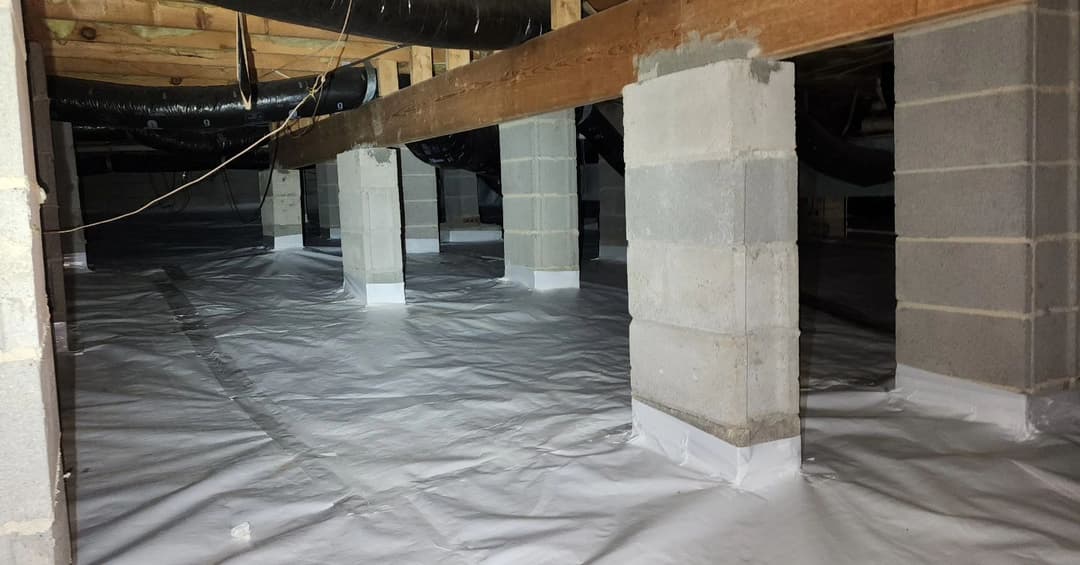 Crawl space with concrete pillars and moisture barrier covering the ground.