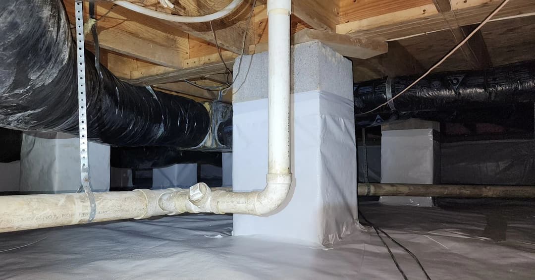 Crawl space with black ductwork and white vapor barrier covering the ground and walls.