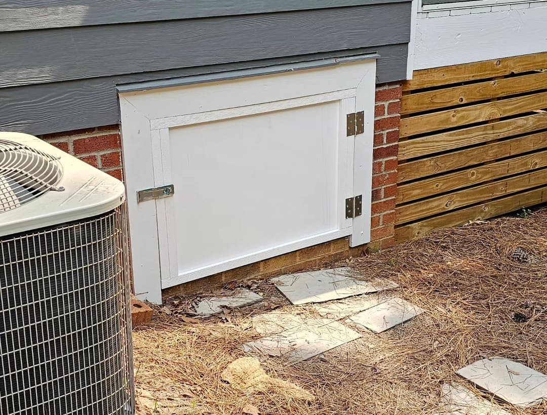 White access door on a house exterior, surrounded by stone path and air conditioner unit.