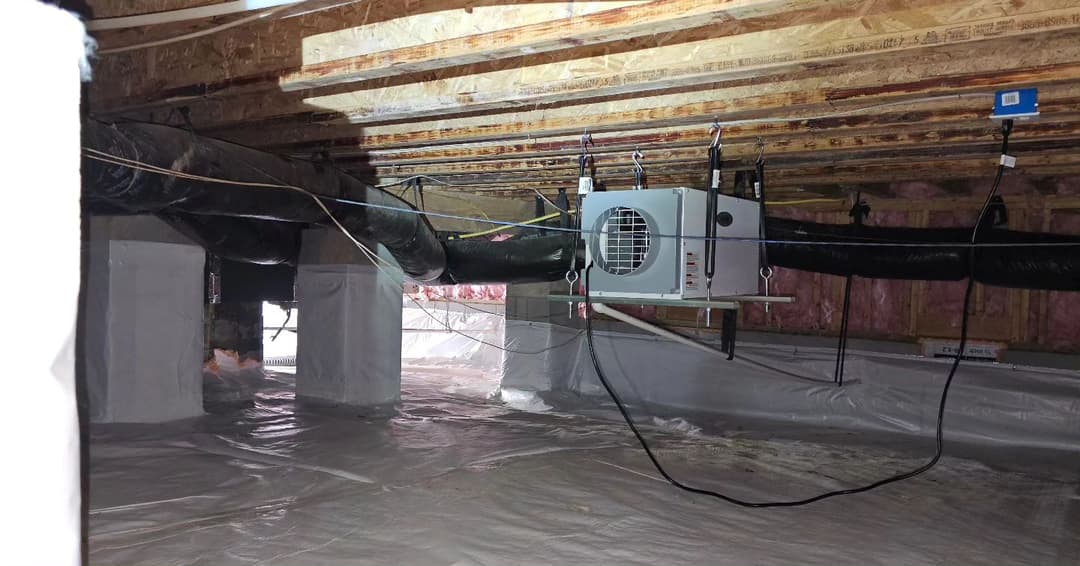 Crawl space with ventilation system, insulated walls, and moisture barrier installed.