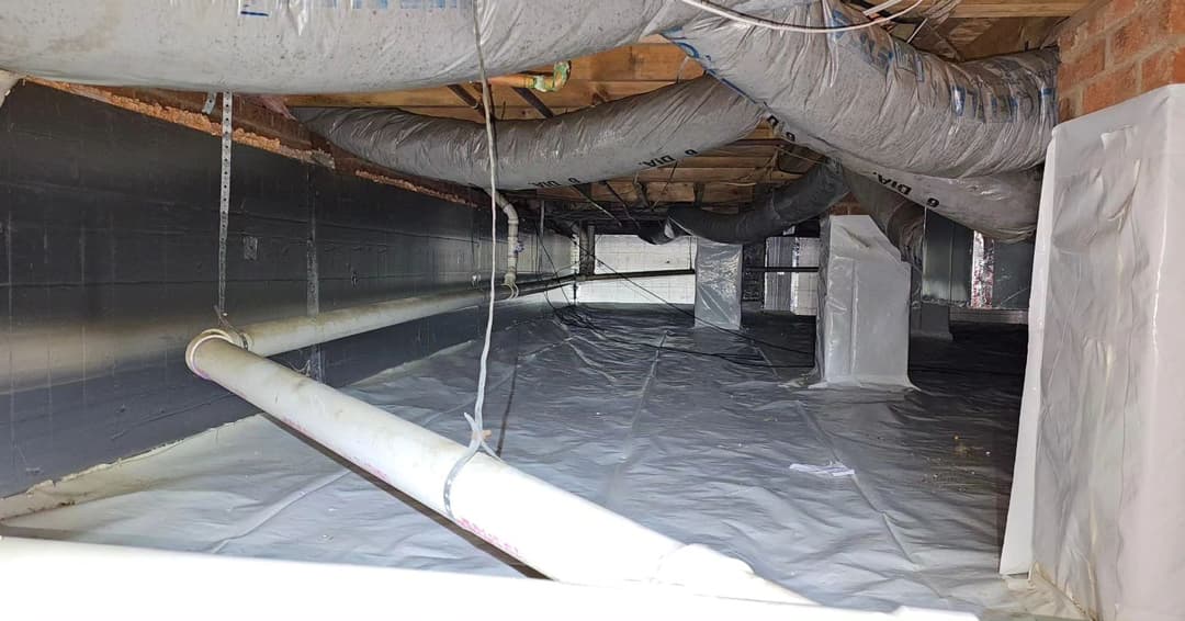 Under-construction crawl space with insulated ducts and plastic lining for moisture control.