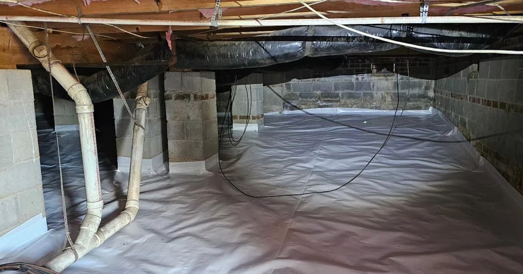 Crawl space with plastic vapor barrier, exposed ductwork, and plumbing pipes.