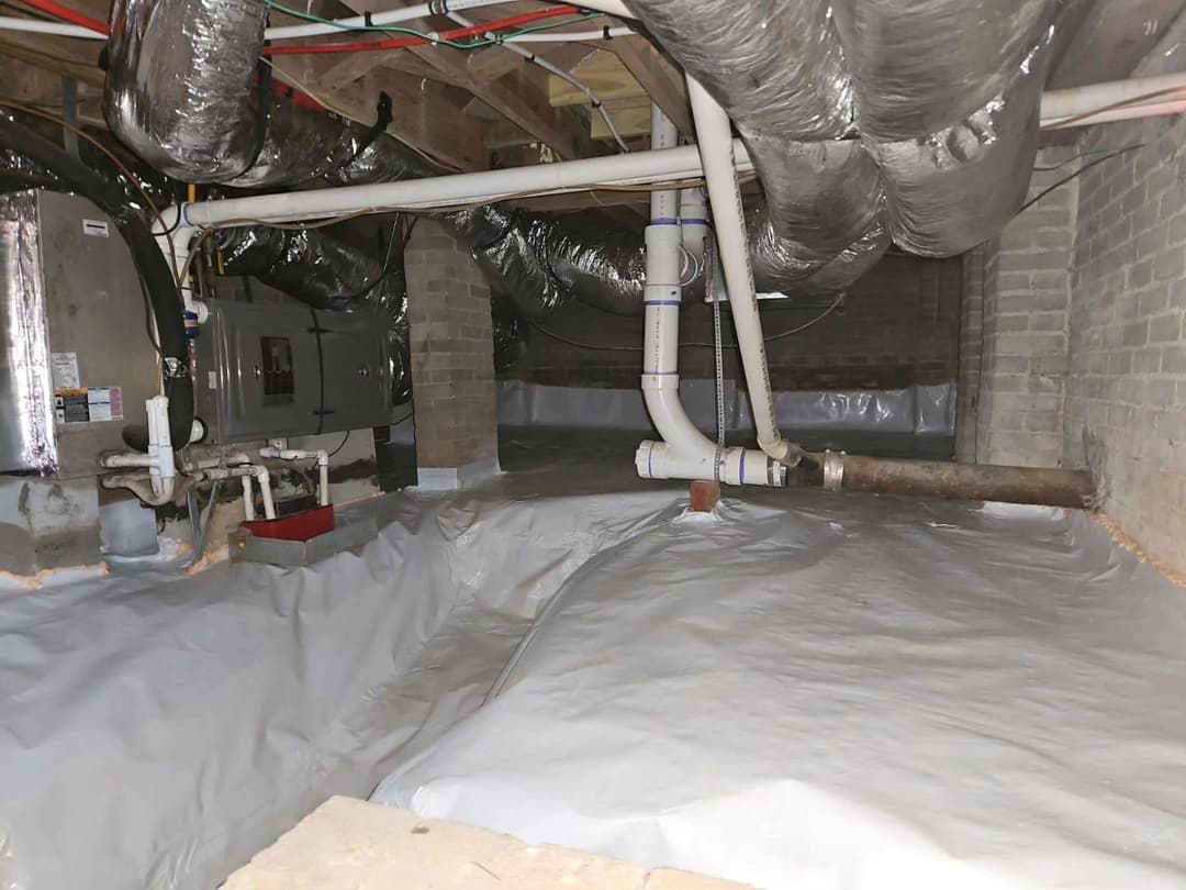 Crawl space with moisture barrier, pipes, and ventilation ducts for home maintenance.