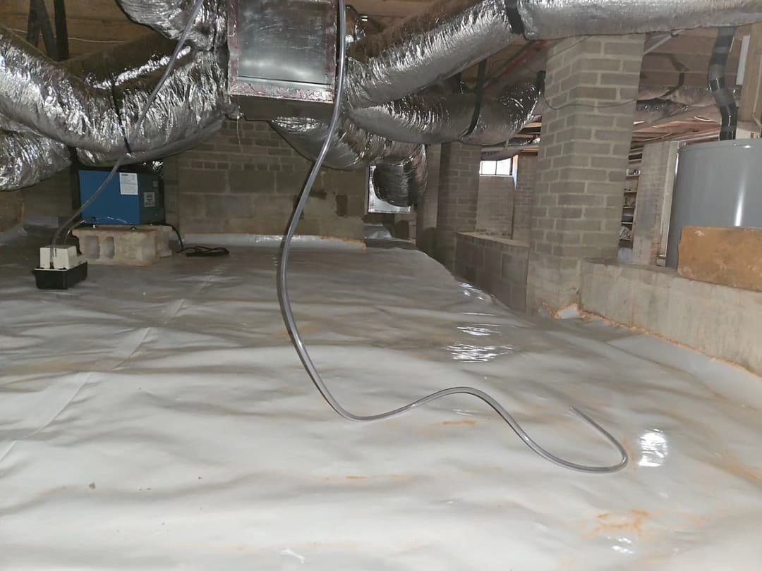Clean and insulated crawl space with ductwork and a sump pump for moisture control.
