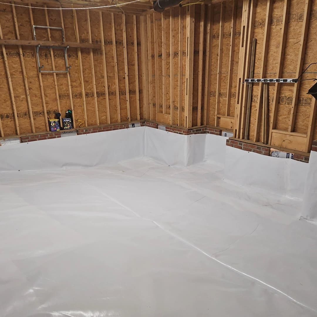 Finished basement with white waterproofing membrane and exposed wooden framing.