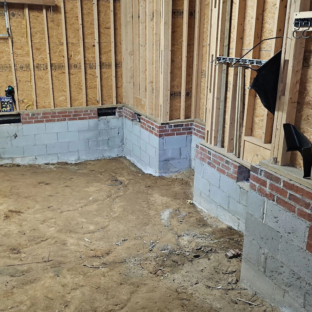 Interior construction site showing unfinished walls with brick and concrete foundations.