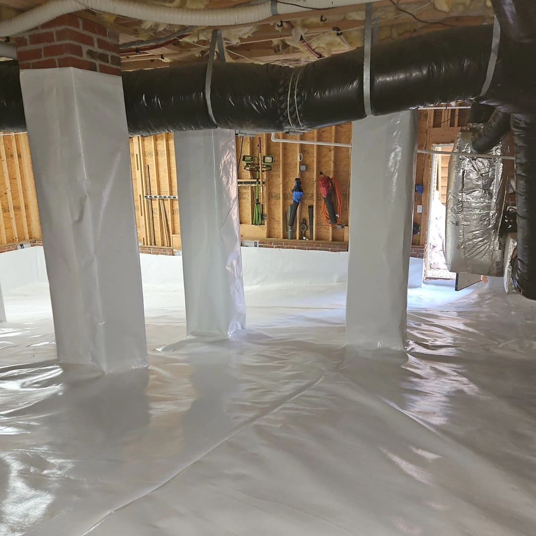 Clean basement with white vapor barrier and exposed wooden framing, showcasing insulation and pipes.