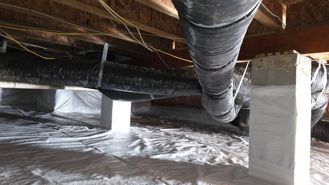 Insulated black ducts under a house, surrounded by a plastic vapor barrier.