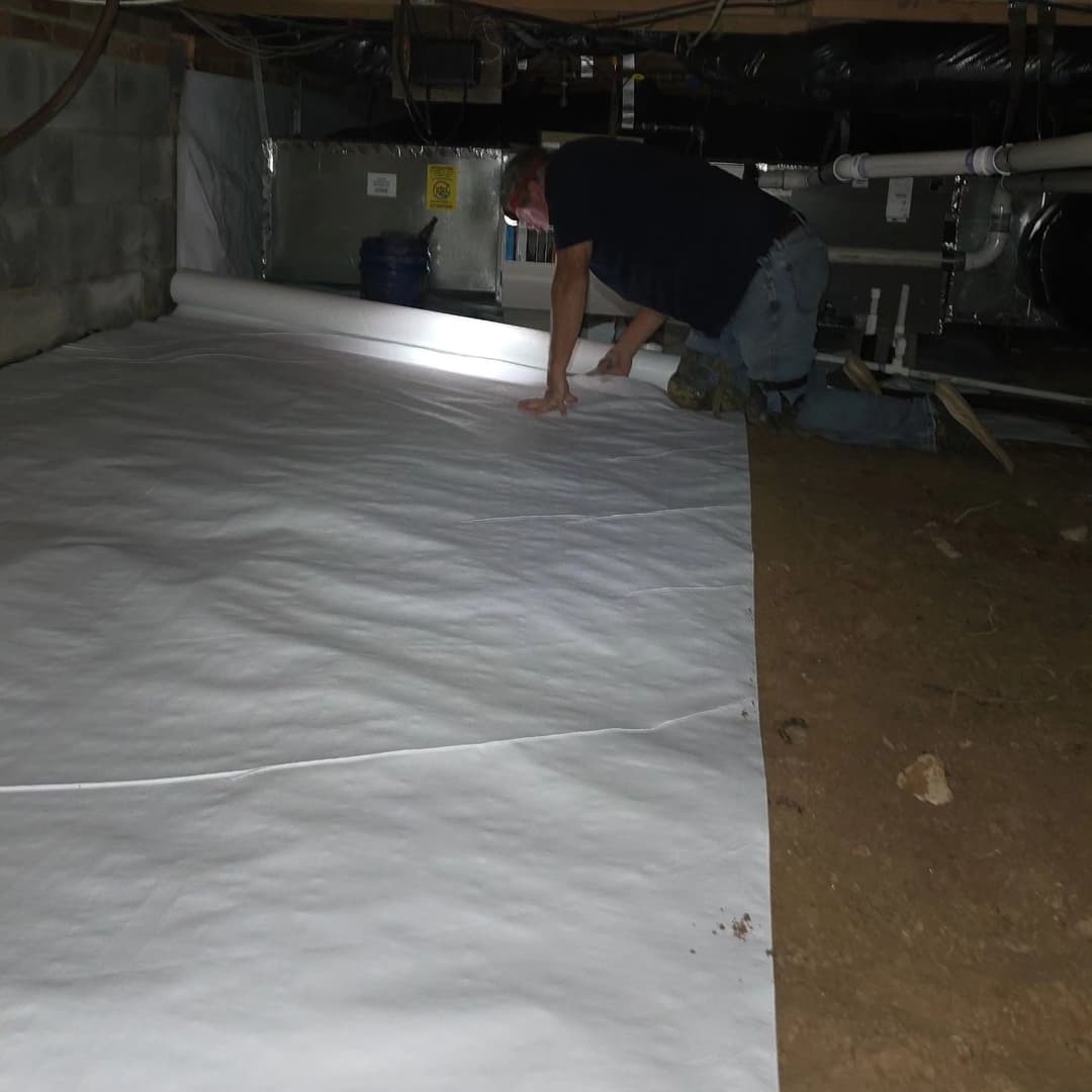 Man installing plastic vapor barrier in a basement to prevent moisture damage.