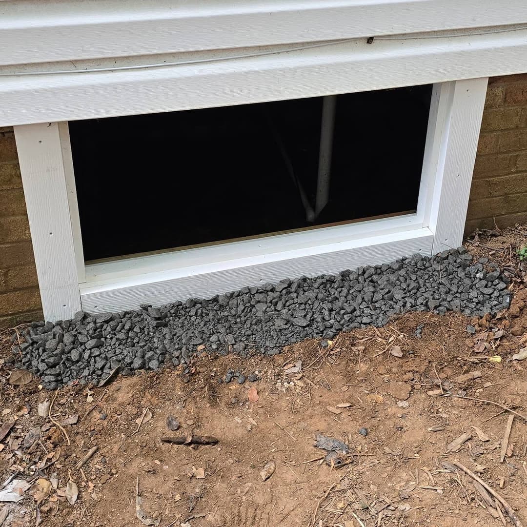 Window well filled with gravel, ensuring drainage and preventing water damage beneath a house.