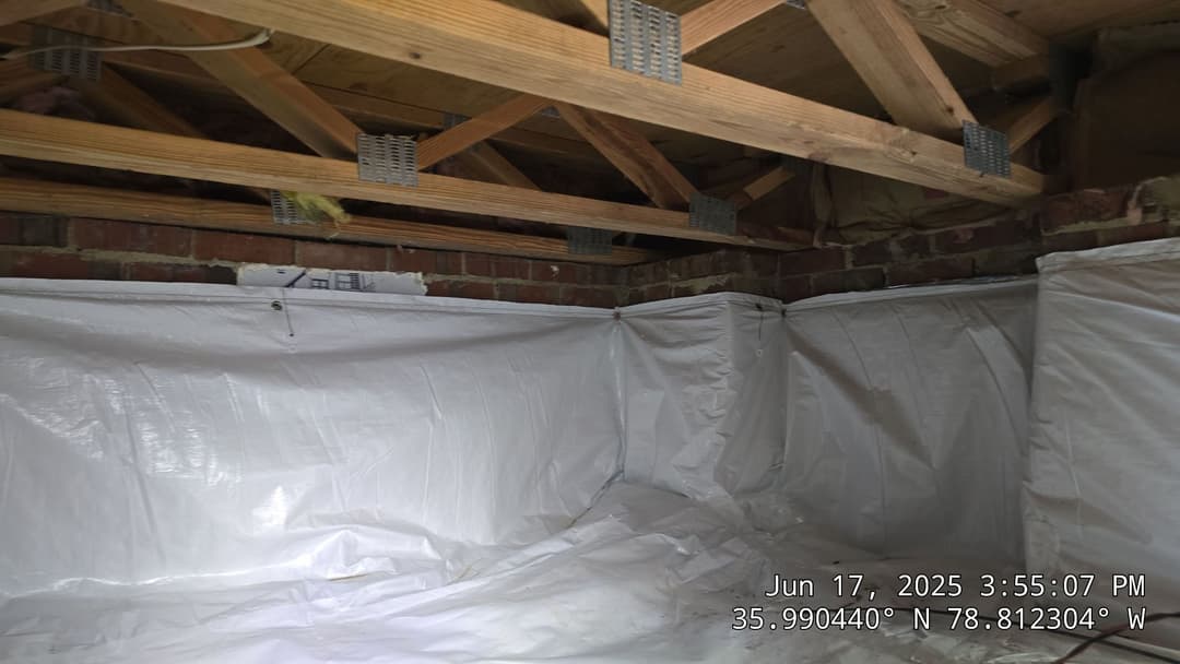 Crawl space with plastic sheeting and wooden beams, showing foundation insulation.