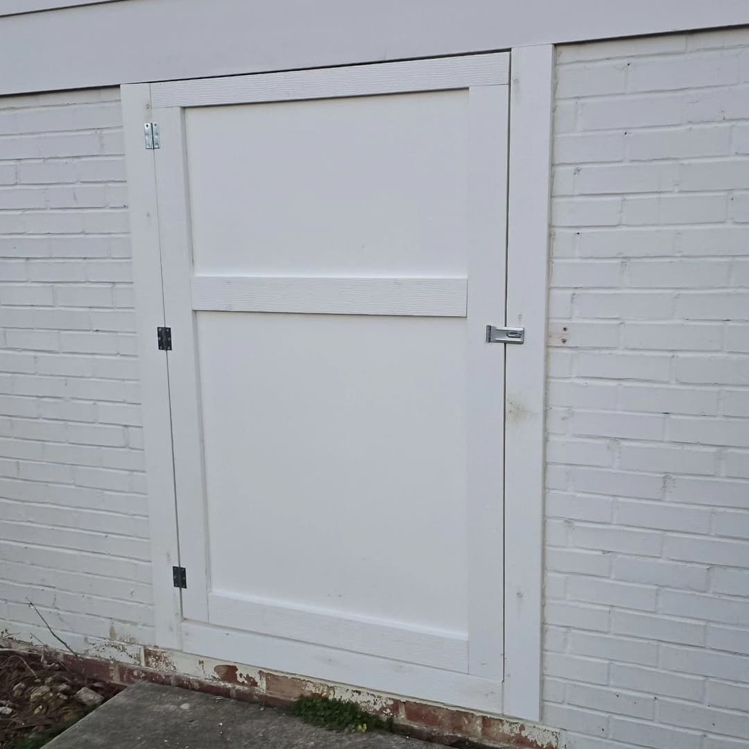 White wooden door with latch on a white brick wall, near a stone pathway.