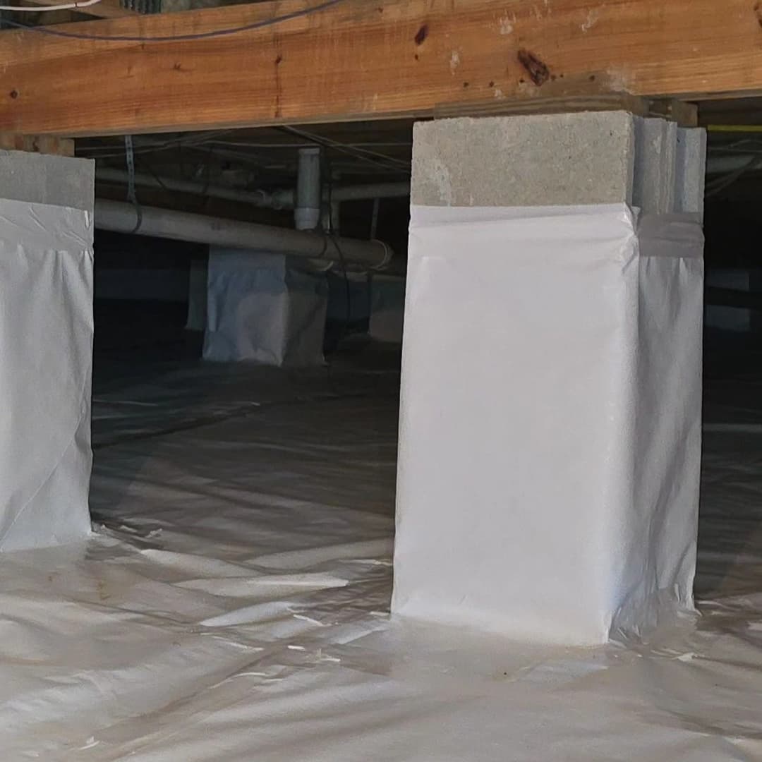 Crawl space with concrete pillars wrapped in plastic sheeting for moisture control.