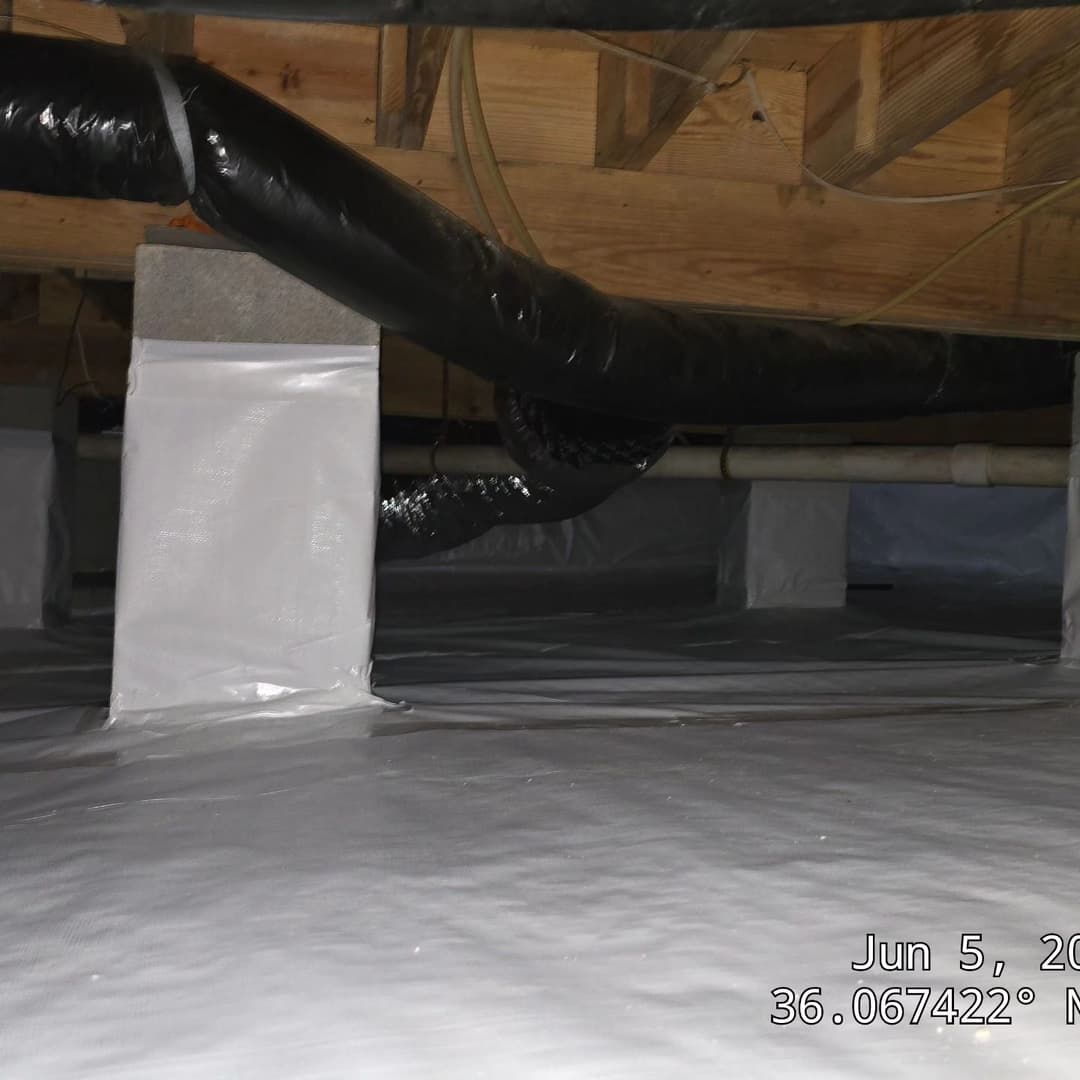 Crawl space with black piping and moisture barrier installation on the floor.