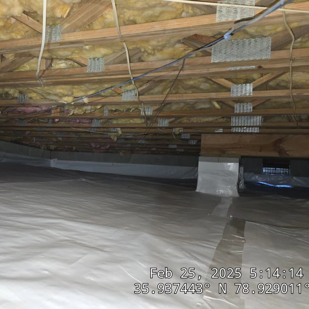 Empty attic space with exposed wooden beams and insulation on the ceiling, showing vapor barrier.