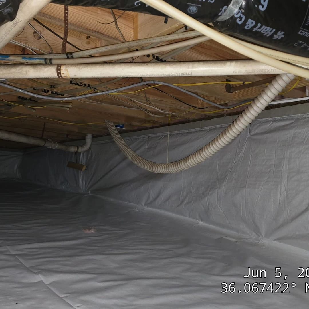 Crawl space with white vapor barrier and exposed plumbing and electrical lines.