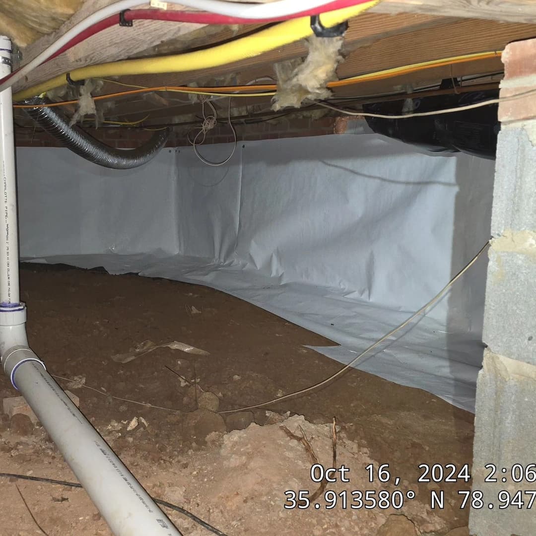Crawl space with white vapor barrier, plumbing, and exposed dirt, Maryland, October 2024.
