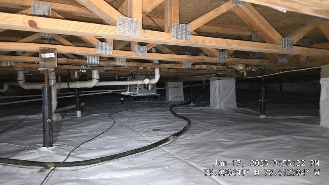 Crawl space with wooden beams, plumbing, and vapor barrier for moisture control.