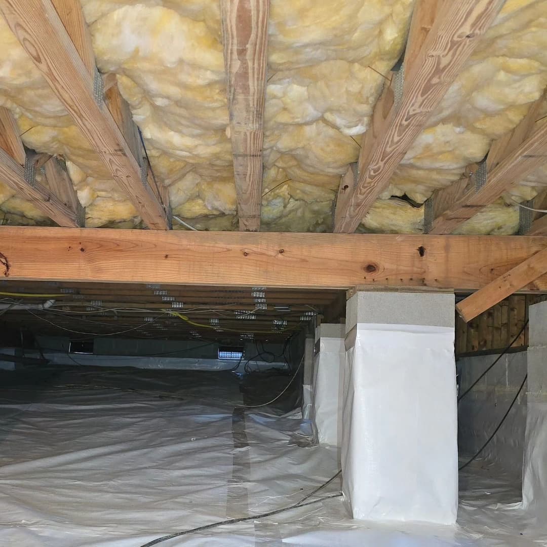Insulated crawl space with wooden beams and vapor barrier for moisture control.