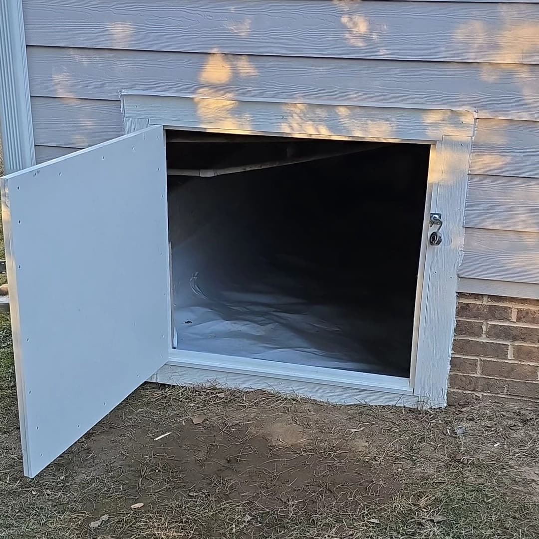 Opened basement access door revealing a clean, empty crawl space under a house.