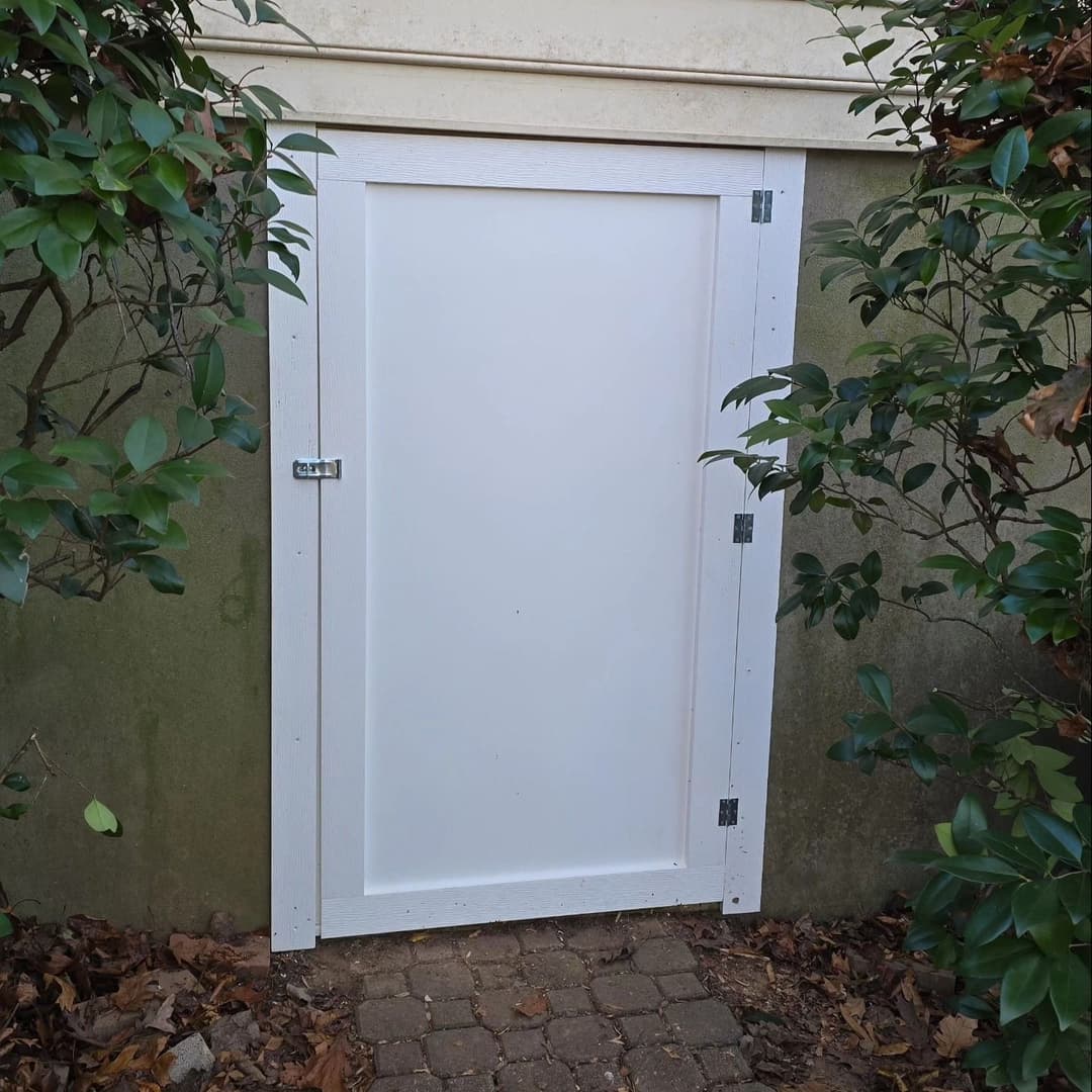 White outdoor storage door framed by greenery and laid stone pathway.