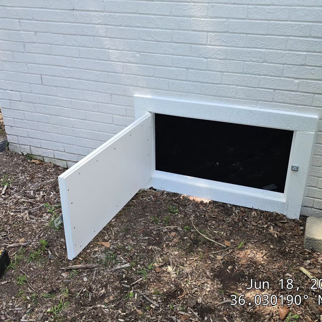 White access door for a crawl space on a brick exterior wall, partially open.